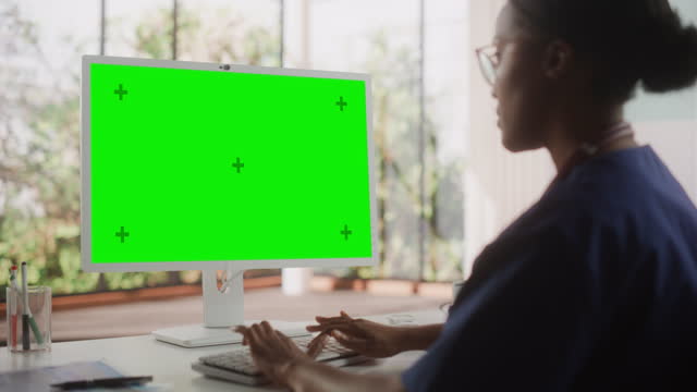 African Healthcare Nurse Using Desktop Computer with Green Screen Chroma Key Display for Day-to-Day Hospital Operations. Beautiful Young Clinic Professional Using PC for Online Medical Work