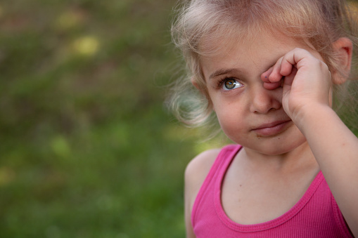 Close-up of a child looking up and rubbing her eye