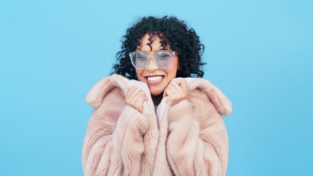 Fashion, fur coat and face of woman with smile on blue background for happy, beauty and laughing. Luxury style, clothes and portrait of excited girl with trendy, stylish and sunglasses in studio