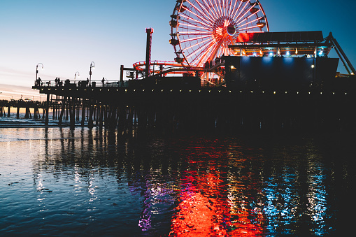 Glowing lights of brightly illuminated Ferris wheel located on pier against sunrise sky in morning in Santa Monica in California