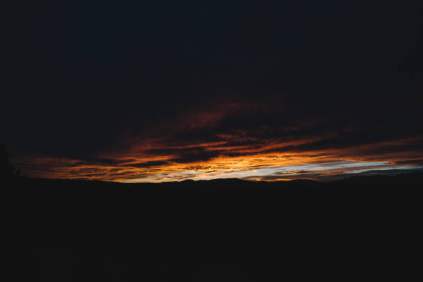 Minimalist landscape of burning line of golden amazing sunset illuminating black clouds in dark sky at evening time in nature