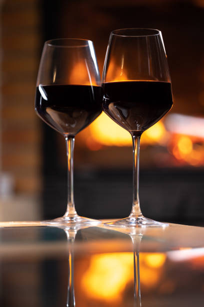 istock two glasses of red wine placed on a table with a fireplace in the background. Reflection of glasses on the table. Concept of conviviality at aperitif time 1473960105