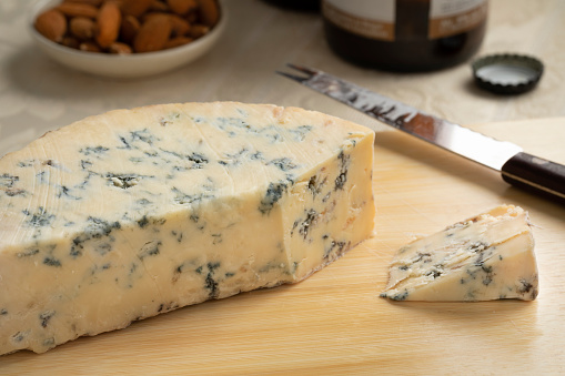 Piece of traditional English Stilton blue cheese and a piece close up on a cutting board