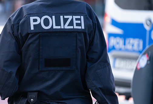 Rear View Of Police Officer On City Street Against Police Car