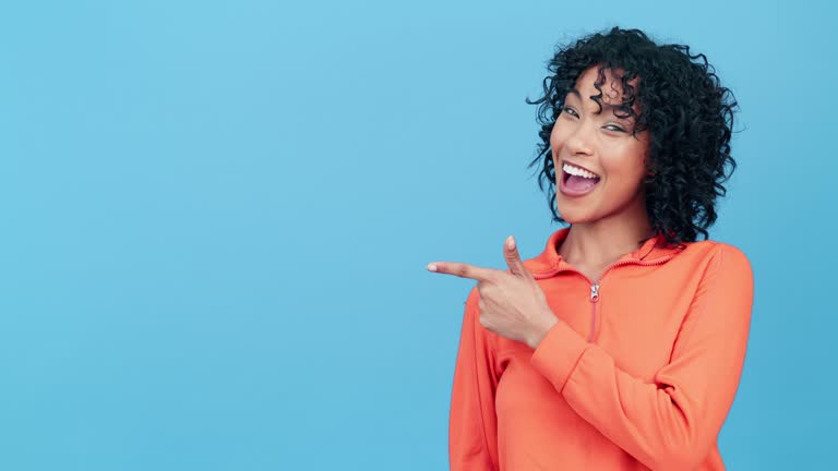 Face, woman and pointing to mockup, blue background and advertising studio space. Portrait of happy model show mock up marketing, news promotion and product placement deal for sales offer coming soon