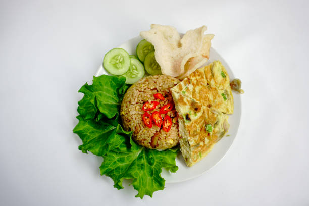 Nasi goreng or fried rice served with egg, prawn crackers, chicken drumstick, lettuce and cucumber slices. Nasi Goreng is an Indonesian cuisine dish. Balinese Food. Asian meal. Top view