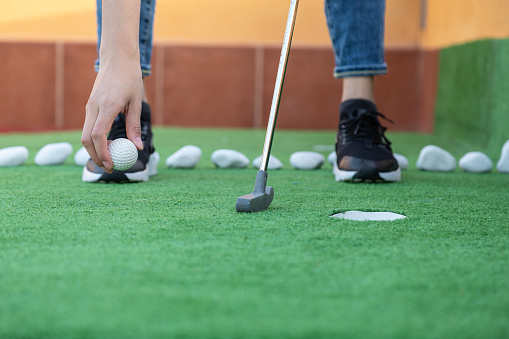 Close-up of unrecognisable woman putting golf ball on the ground playing mini golf