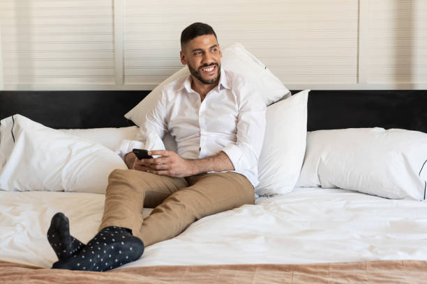 istock Businessman lying in a hotel bed while thinking and smiling after reading a message on his smartphone 1473968638