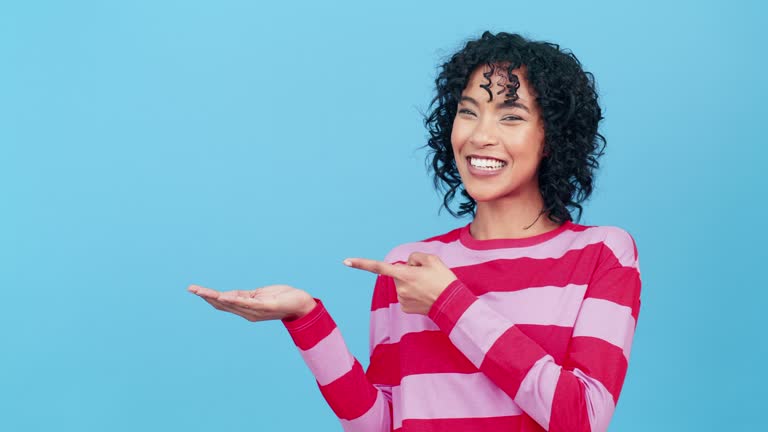Woman, pointing and mockup on blue background for advertising studio, color space or marketing. Portrait of happy model show mock up, news promotion or review branding deal of sales offer coming soon
