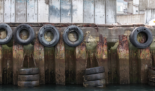 Grungy mooring wall with rubber bumpers made of old used car tyres. Close up photo, front view
