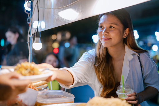 A young Asian woman receiving her order from a street food stall in a night market.