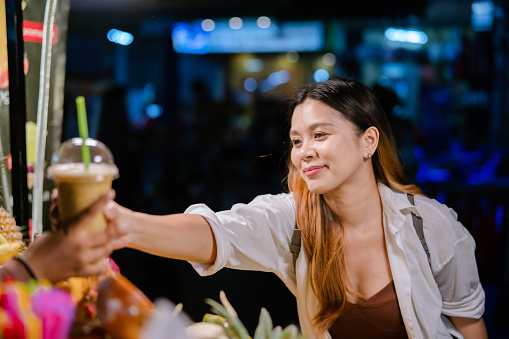 A young Asian woman receiving her order from a blended drink stall in a night market.