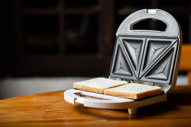 istock Sandwich maker with prepared toast on wooden table on dark background. Place for text. 1473977520
