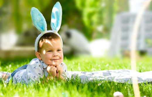 A happy smiling little boy with rabbit ears on his head. Easter photo, festive green background with a little smiling boy. Bright festive Sunday.