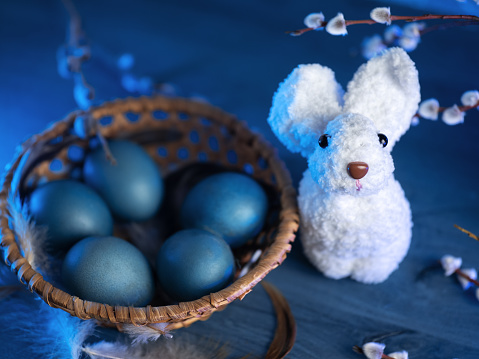 Easter composition with a white knitted bunny and a basket of eggs on a blue background