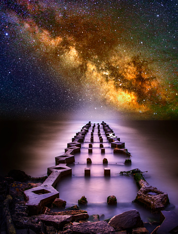 Mystical ruins of ancient structure reach out into misty sea under the Milky Way Galaxy.