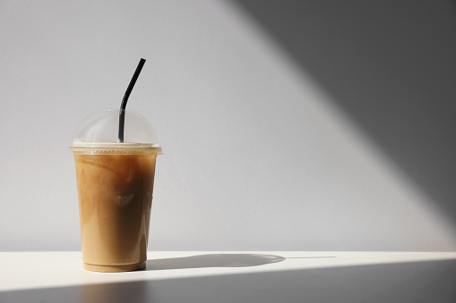 Plastic takeaway cup of delicious iced coffee on white table under sunlight, space for text