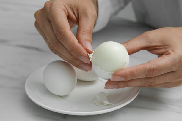istock Woman peeling boiled egg at white marble table, closeup 1473989793