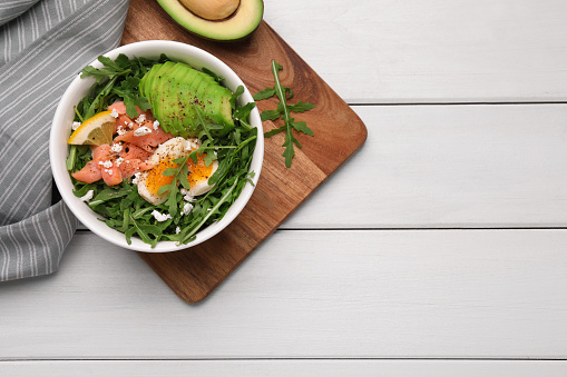 Delicious salad with boiled egg, salmon and avocado served on white wooden table, flat lay. Space for text