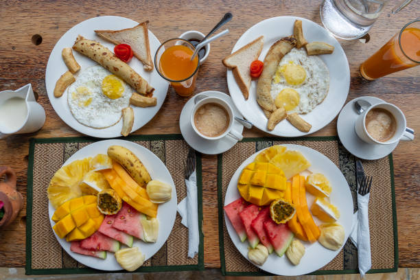 istock Tropical breakfast of fruit, coffee and scrambled eggs and banana pancake for two on the beach near sea. Top view, table setting. 1473991021