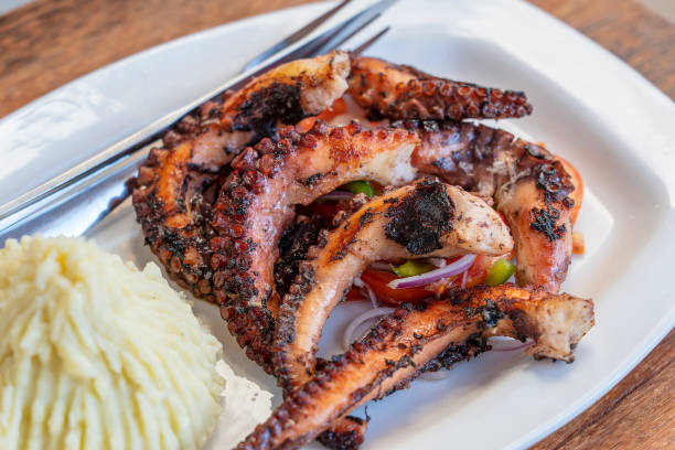 istock Fried octopus tentacles with mashed potato and vegetable salad on a plate, close up 1473991114