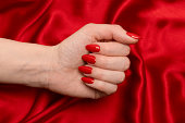 Red manicure on woman hands on a luxury red silk backround.