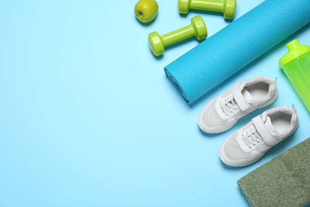 istock Exercise mat, dumbbells, apple, towel, shaker and shoes on light blue background, flat lay. Space for text 1473991580