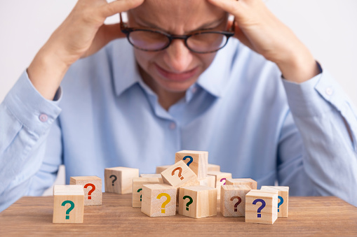 Close-up shot of a businesswoman having a hard time while making a decision. She is experiencing a headache during the work. There are question marks on wooden cubes.