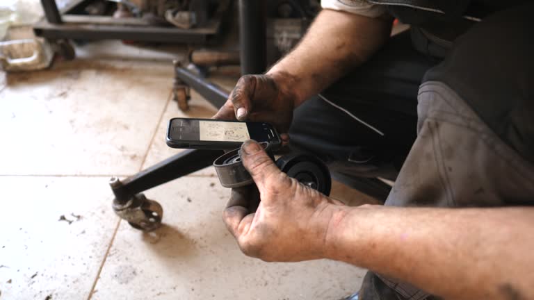 Auto mechanic inspecting new vehicle part and installation instruction on smartphone. Repairman checking manual to car detail on his phone before work. Concept of automobile maintenance. Close up