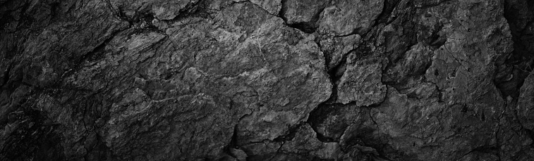 Cracked rock texture. Black white stone background. Grunge. Dark gray rough surface. Close-up. Broken, damaged, collapsed. Wide banner. Panoramic.