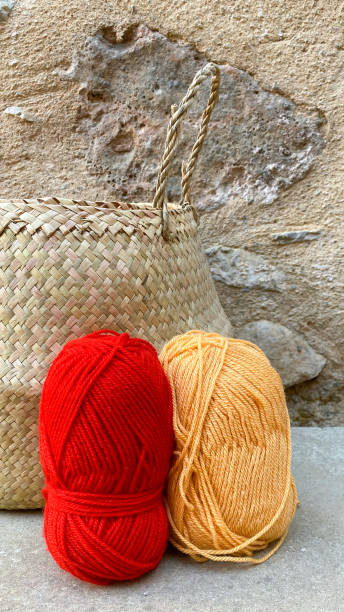 Still life with two balls of wool: one red and one orange and a straw basket Still life with two balls of wool: one red and one orange and a straw basket sewing thread rolled up creation stock pictures, royalty-free photos & images