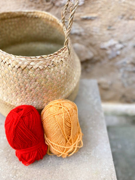 Still life with two balls of wool: one red and one orange and a straw basket Still life with two balls of wool: one red and one orange and a straw basket sewing thread rolled up creation stock pictures, royalty-free photos & images