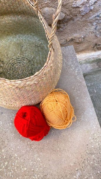 Still life with two balls of wool: one red and one orange and a straw basket Still life with two balls of wool: one red and one orange and a straw basket sewing thread rolled up creation stock pictures, royalty-free photos & images