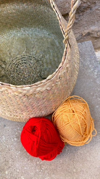 Still life with two balls of wool: one red and one orange and a straw basket Still life with two balls of wool: one red and one orange and a straw basket sewing thread rolled up creation stock pictures, royalty-free photos & images