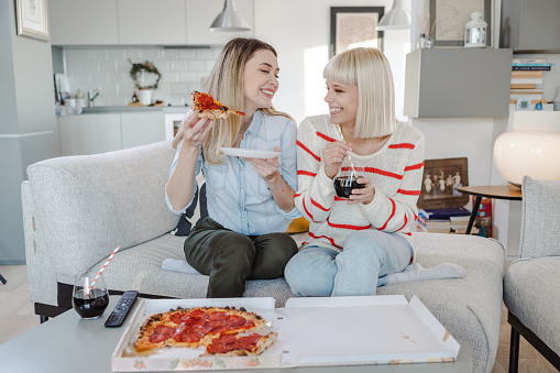 Two young blonde woman talking and eating pizza