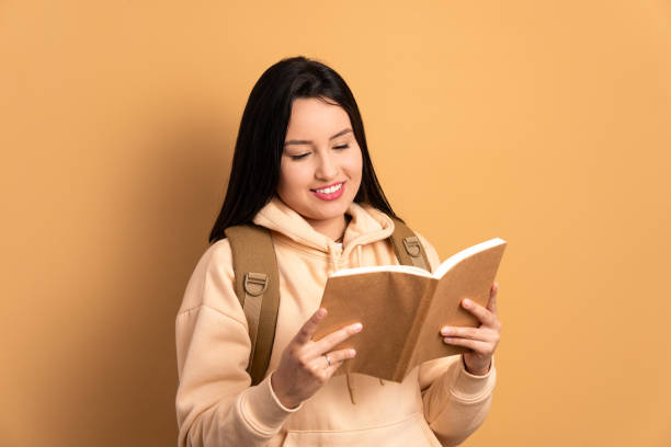 istock joyful female student reading book to study in beige colors. learn, school, student life concept. 1474003393