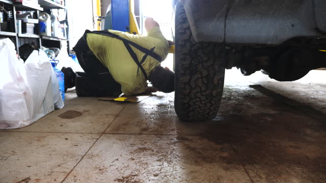 Auto mechanic controls process of lifting car on a lift at garage. Repairman working with broken vehicle at workshop. Preparation for diagnostic automobile at service. Concept of transport maintenance