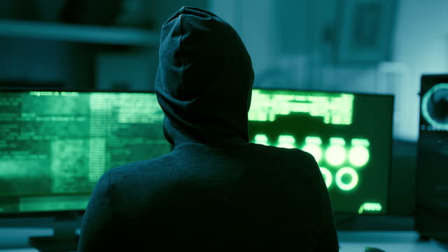Hacker, coding and computer screen for cyber attack, security virus or malicious software at night. Mysterious unknown user black hat hacking on desktop PC or AI app for theft or fraud in dark room