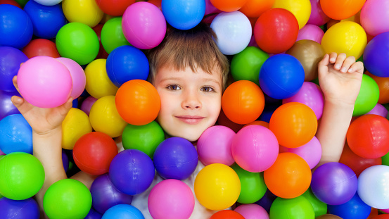 Colorful balls dry pool kindergarten playground child indoor play area. Playroom kids ball pit. Caucasian boy indoor playground kids play zone or kids zone. Smile kid lying colorful plastic balls pool