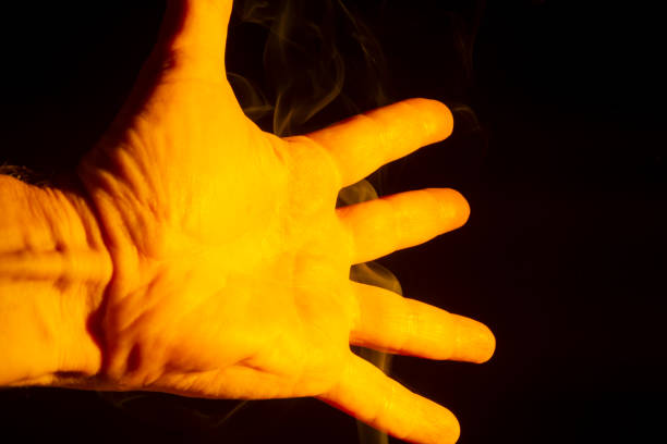 A male hand lit yellow with smoke around it isolated on a black background.