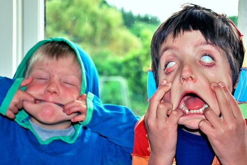 Two pre-school age children pull faces at camera.