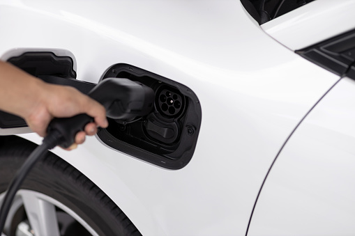 Closeup focus hand insert EV charger plug to electric vehicle from charging station. Progressive alternative clean energy engine car technology. Renewable EV car for eco-friendly transportation idea.