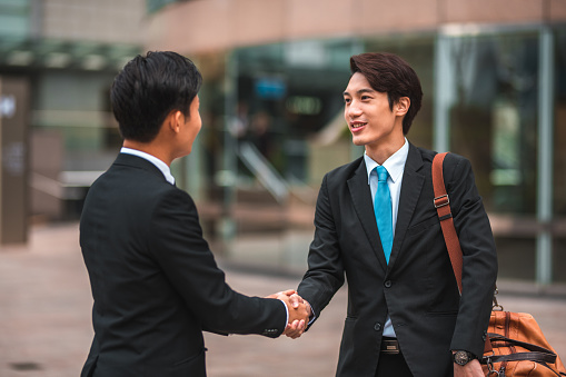 Formal greeting. Waist up shot of two good looking chinese businessmen holding hands at an outdoor meeting.