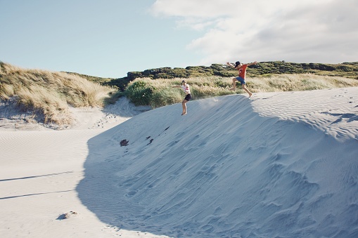 Two boys jump in the air from a sand dune at a beach in summer..