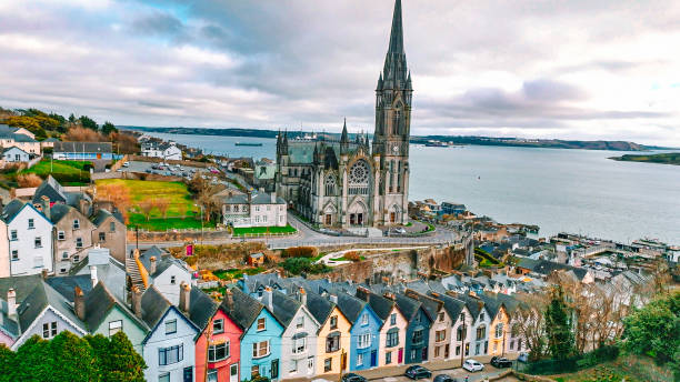 Aerial view of the Cathedral and colored houses in Cobh, Ireland ,colorful houses and St Colman's Cathedral in Cobh, Houses and catherdral in Cobh, colorful town Cobh, known from 1849 until 1920 as Queenstown, is a seaport town on the south coast of County Cork, Ireland. With a population of around 13,000 inhabitants, Cobh is on the south side of Great Island in Cork Harbour and home to Ireland's only dedicated cruise terminal. Tourism in the area draws on the maritime and emigration legacy of the town.

Facing the town are Spike and Haulbowline islands. On a high point in the town stands St Colman's, the cathedral church of the Roman Catholic Diocese of Cloyne. It is one of the tallest buildings in Ireland, standing at 91.4 metres. county cork stock pictures, royalty-free photos & images