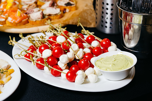 tasty appetizer with mozzarella and cherry tomatoes on skewers and dipping sauce the table. big pile of caprese canapes.