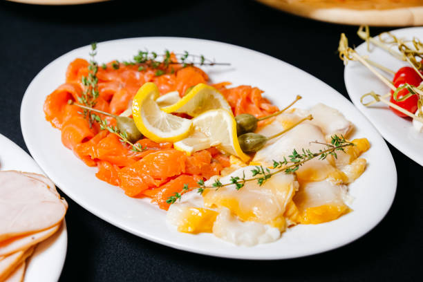 Sliced fillets of fatty fish. Smoked salmon with lemon slices and halibut fillets with large capers. Useful product rich in omega-3. stock photo