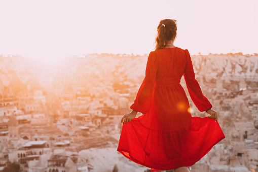 Girl in red dress in Cappadocia watching majestic sunset over a valley with fairy chimney