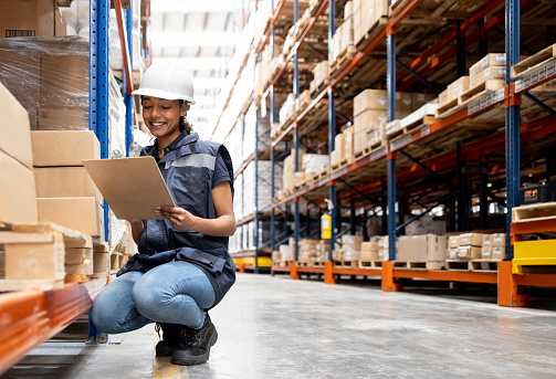 Happy Latin American woman working at a distribution warehouse and smiling while reading notes on her clipboard