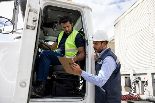 Foreperson talking to a truck driver while working at a distribution warehouse transporting merchandise - freight transportation concepts